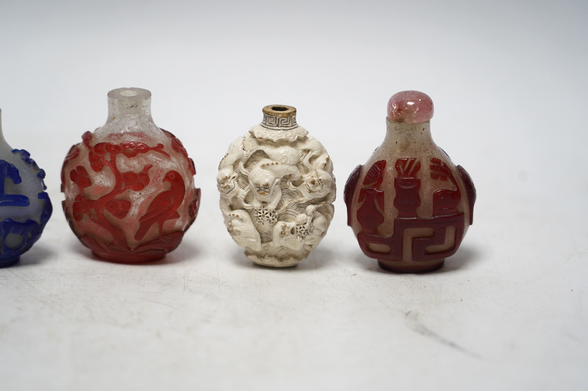 A Chinese moulded and white glazed ‘Buddhist lion’ snuff bottle, 19th century and three overlaid glass snuff bottles 6.5cm high (4)